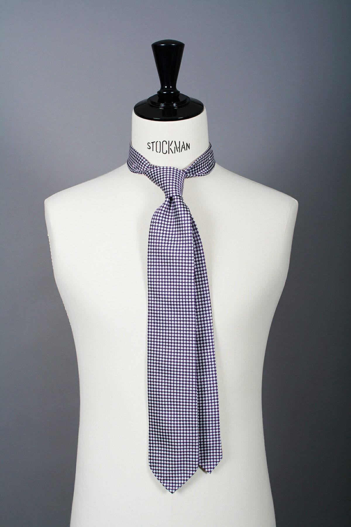 Cravate sartoriale à 3 plis, en soie tissée Jacquard, argentée, motif damier et aperçu du noeud simple sur buste Stockman.