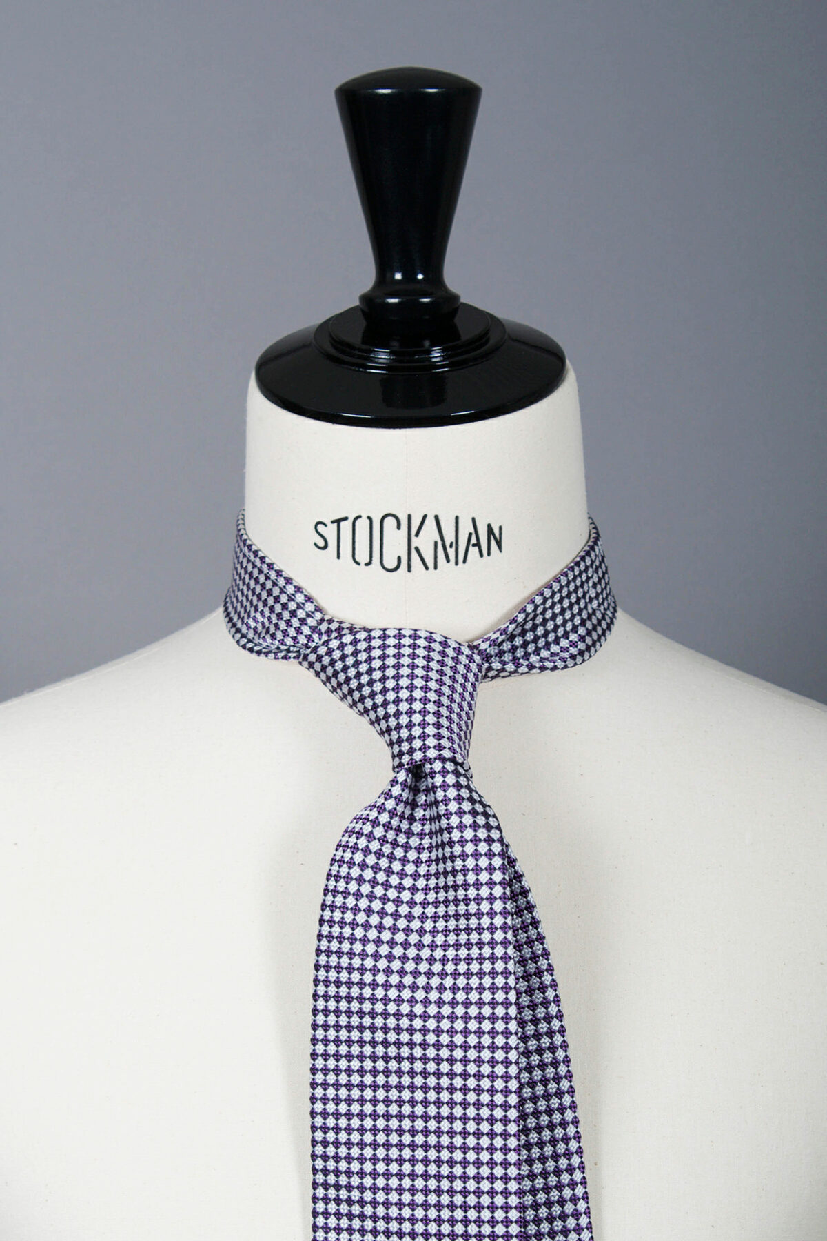 Cravate sartoriale à 3 plis, en soie tissée Jacquard, argentée, motif damier et aperçu du noeud simple sur buste Stockman.