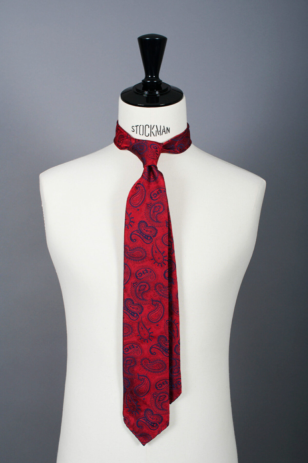 Cravate sartoriale à 3 plis, en soie tissée Jacquard, rouge motif cachemire et aperçu du noeud simple sur buste Stockman.