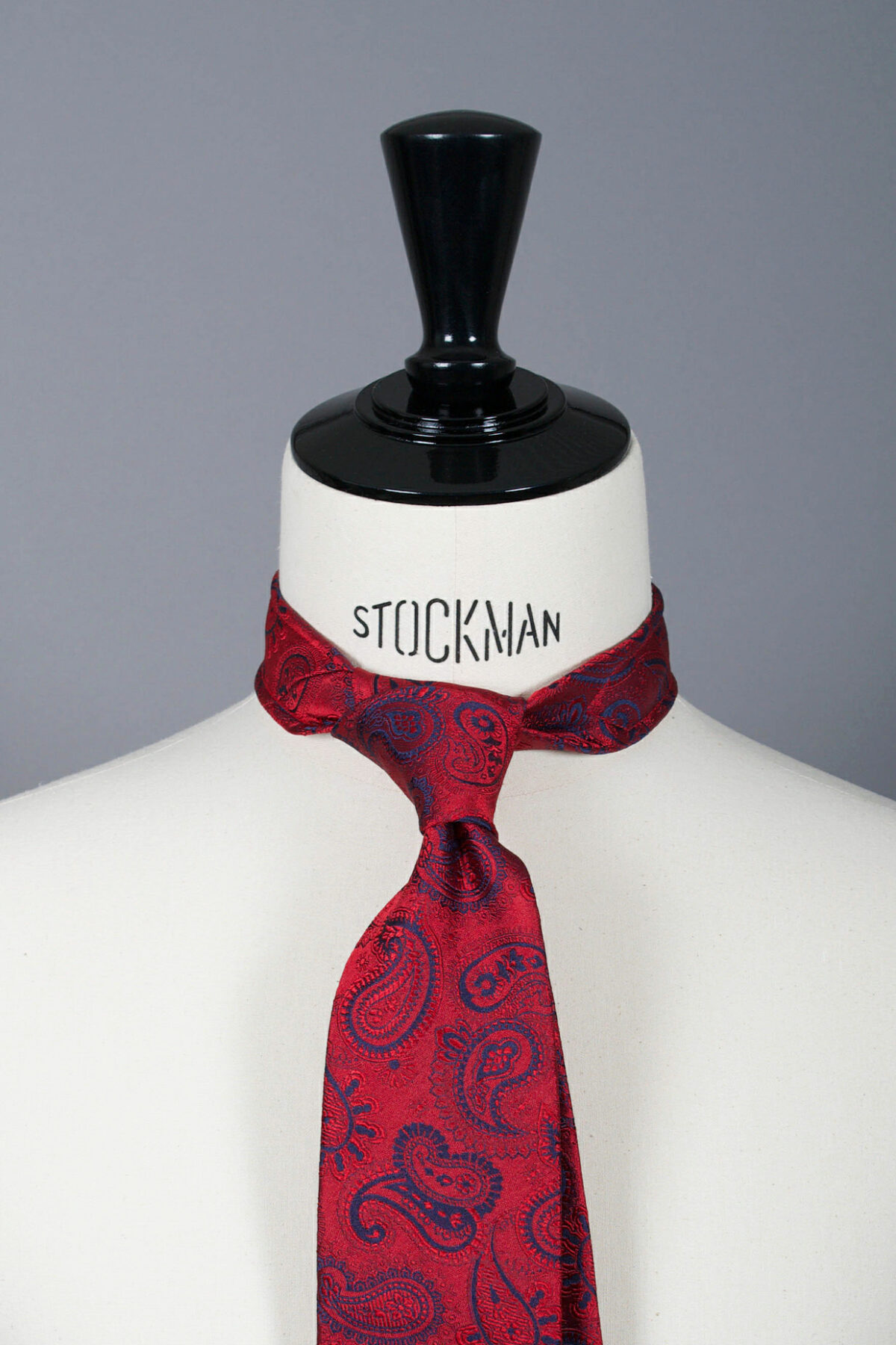 Cravate sartoriale à 3 plis, en soie tissée Jacquard, rouge motif cachemire et aperçu du noeud simple sur buste Stockman.