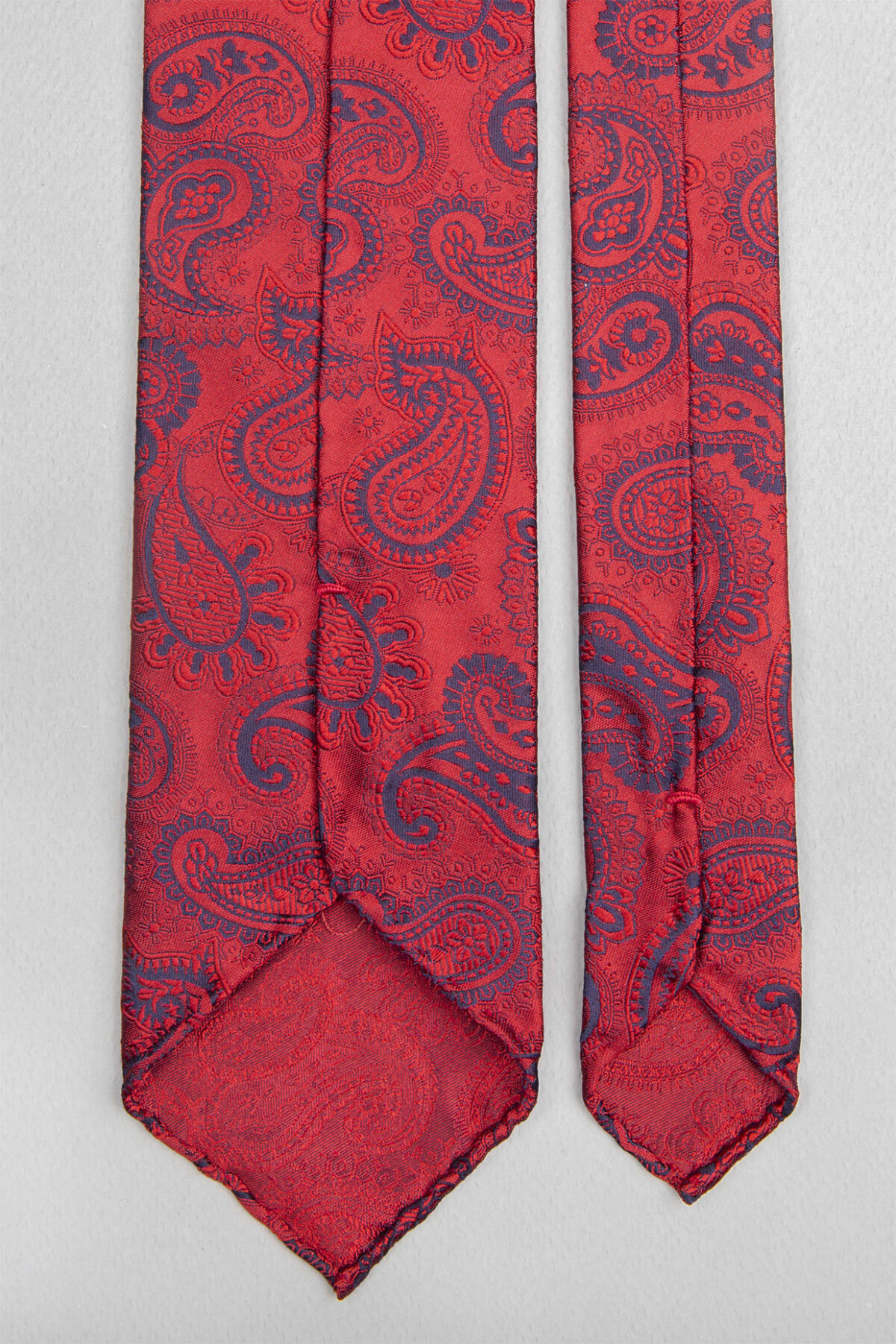 Cravate sartoriale à 3 plis retournée, le roulotté main permet de voir les fils du tissage Jacquard constituant les dessins du modèle.