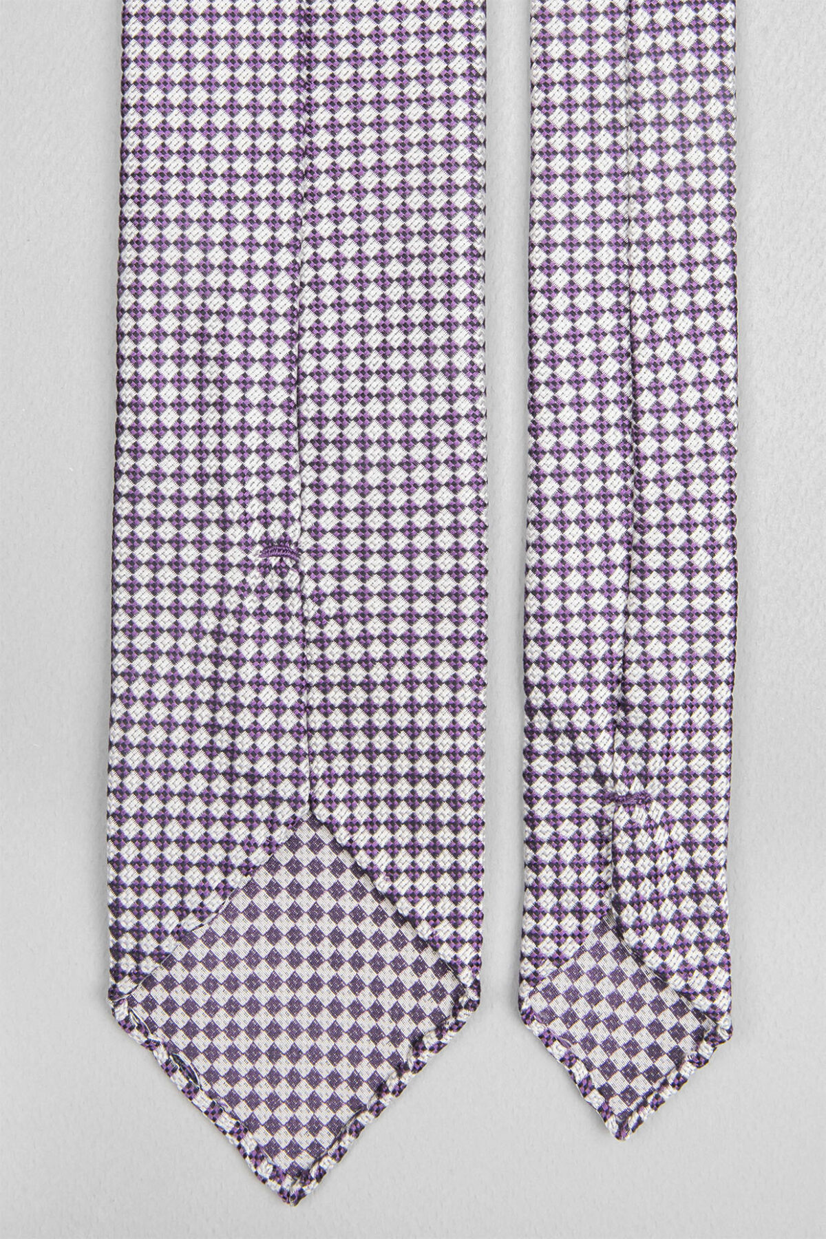 Cravate sartoriale à 3 plis retournée, le roulotté main permet de voir les fils du tissage Jacquard constituant les dessins du modèle.