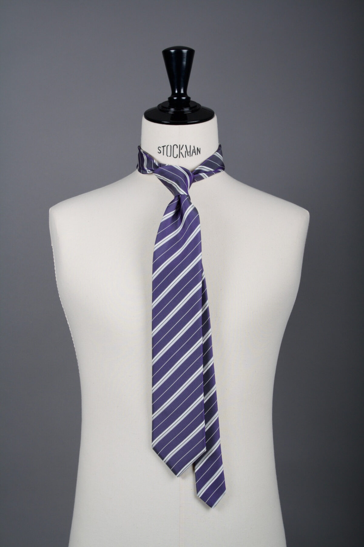 Cravate sartoriale à 3 plis, en soie tissée Jacquard, violette rayures blanches et aperçu du noeud simple sur buste Stockman.