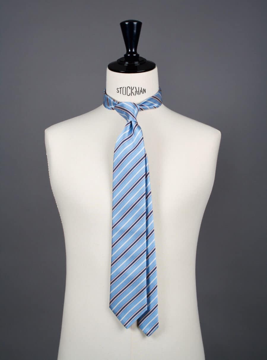 Cravate sartoriale à 3 plis, en soie tissée Jacquard, bleu rayures rouges et blanches et aperçu du noeud simple sur buste Stockman.