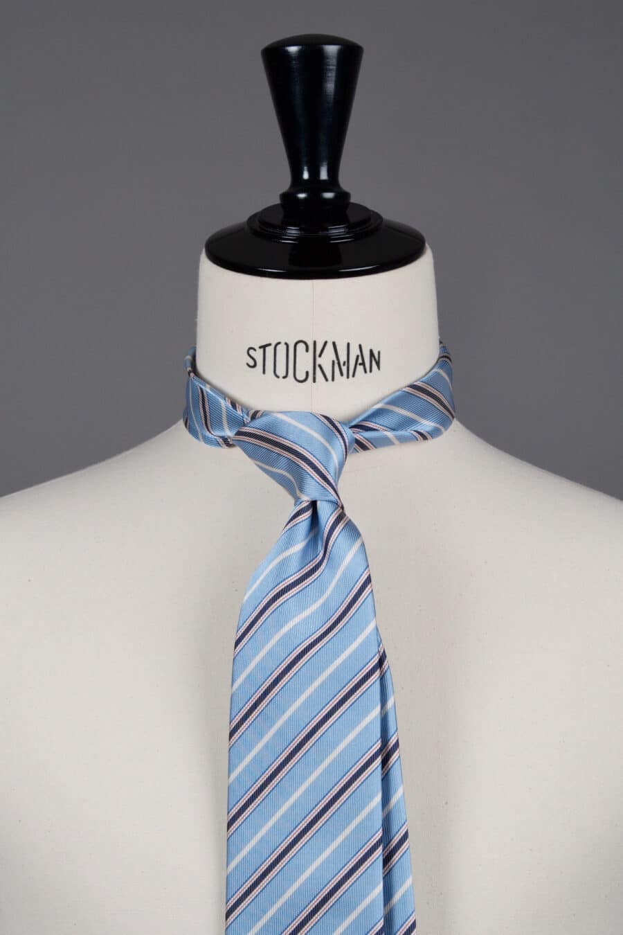Cravate sartoriale à 3 plis, en soie tissée Jacquard, bleu rayures rouges et blanches et aperçu du noeud simple sur buste Stockman.