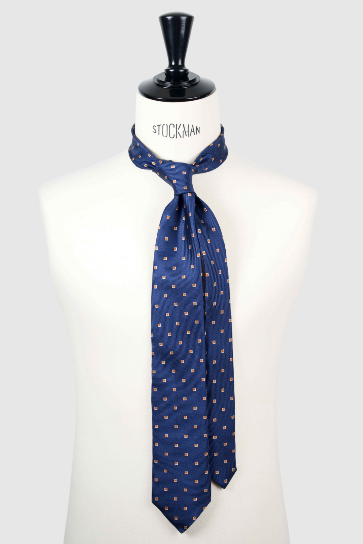 Cravate sartoriale à 3 plis, en soie tissée Jacquard, bleu marine motif géométrique orange et aperçu du noeud simple sur buste Stockman.