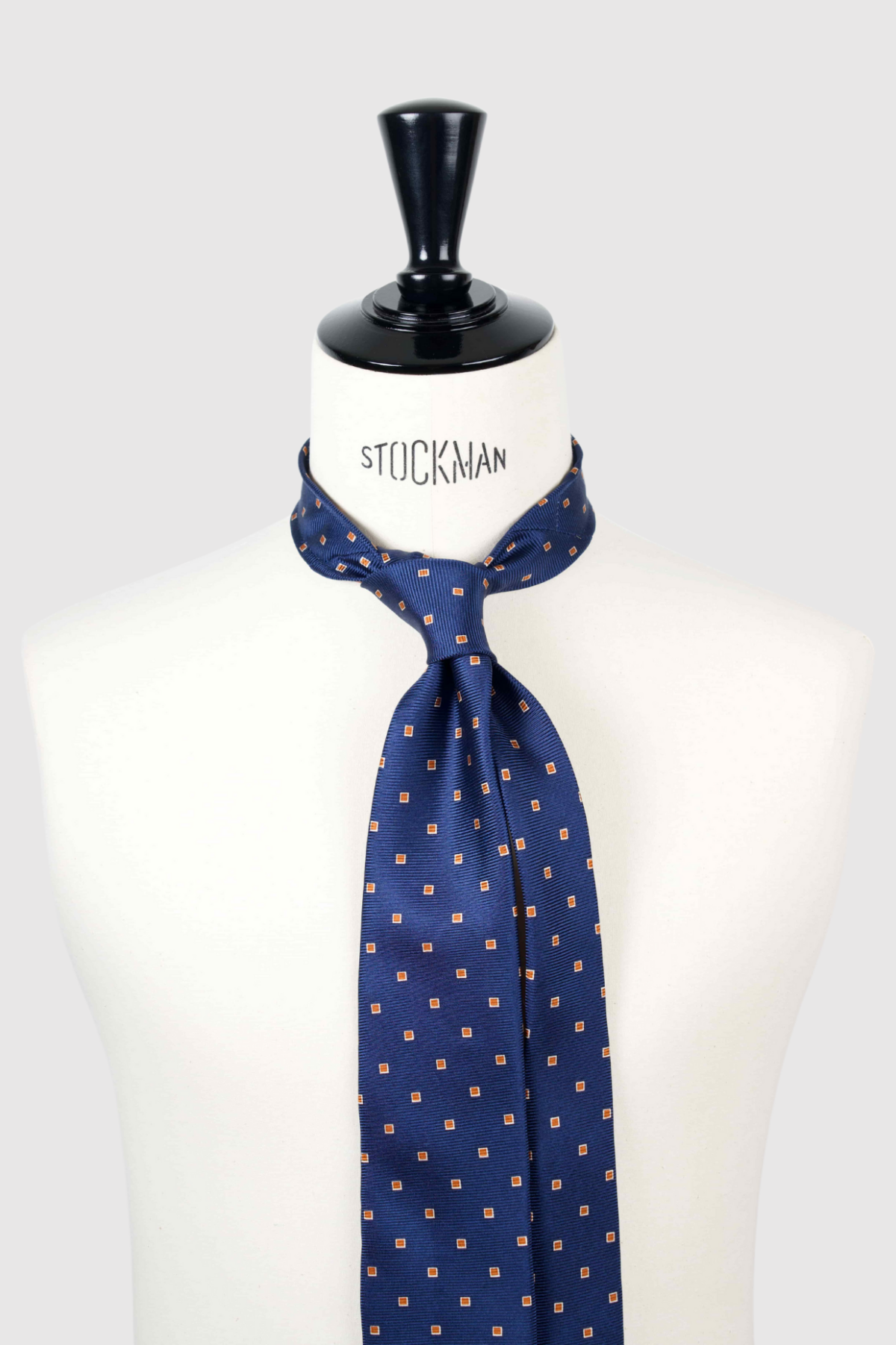 Cravate sartoriale à 3 plis, en soie tissée Jacquard, bleu marine motif géométrique orange et aperçu du noeud simple sur buste Stockman.