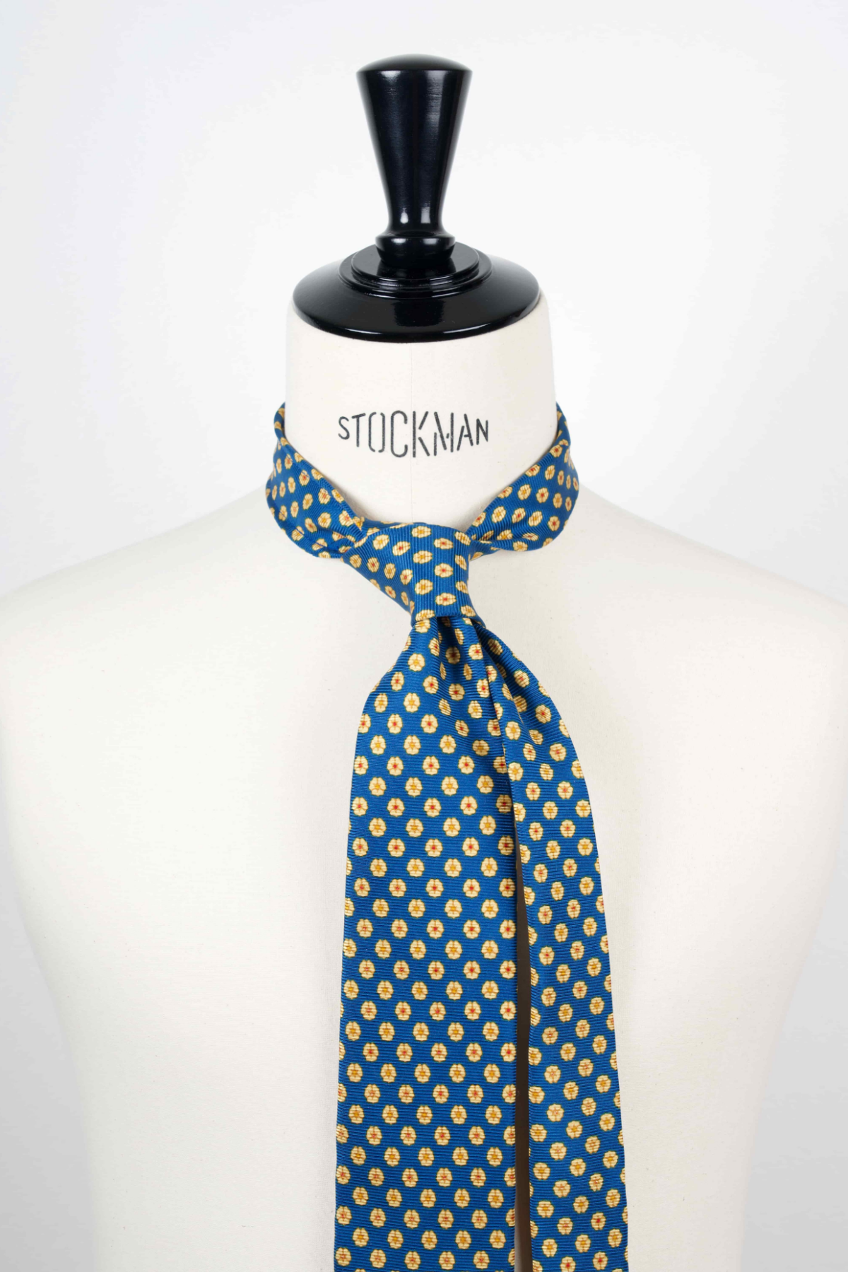 Cravate sartoriale à 3 plis, en soie madder bleu, motif géométrique et aperçu du noeud simple sur buste Stockman.