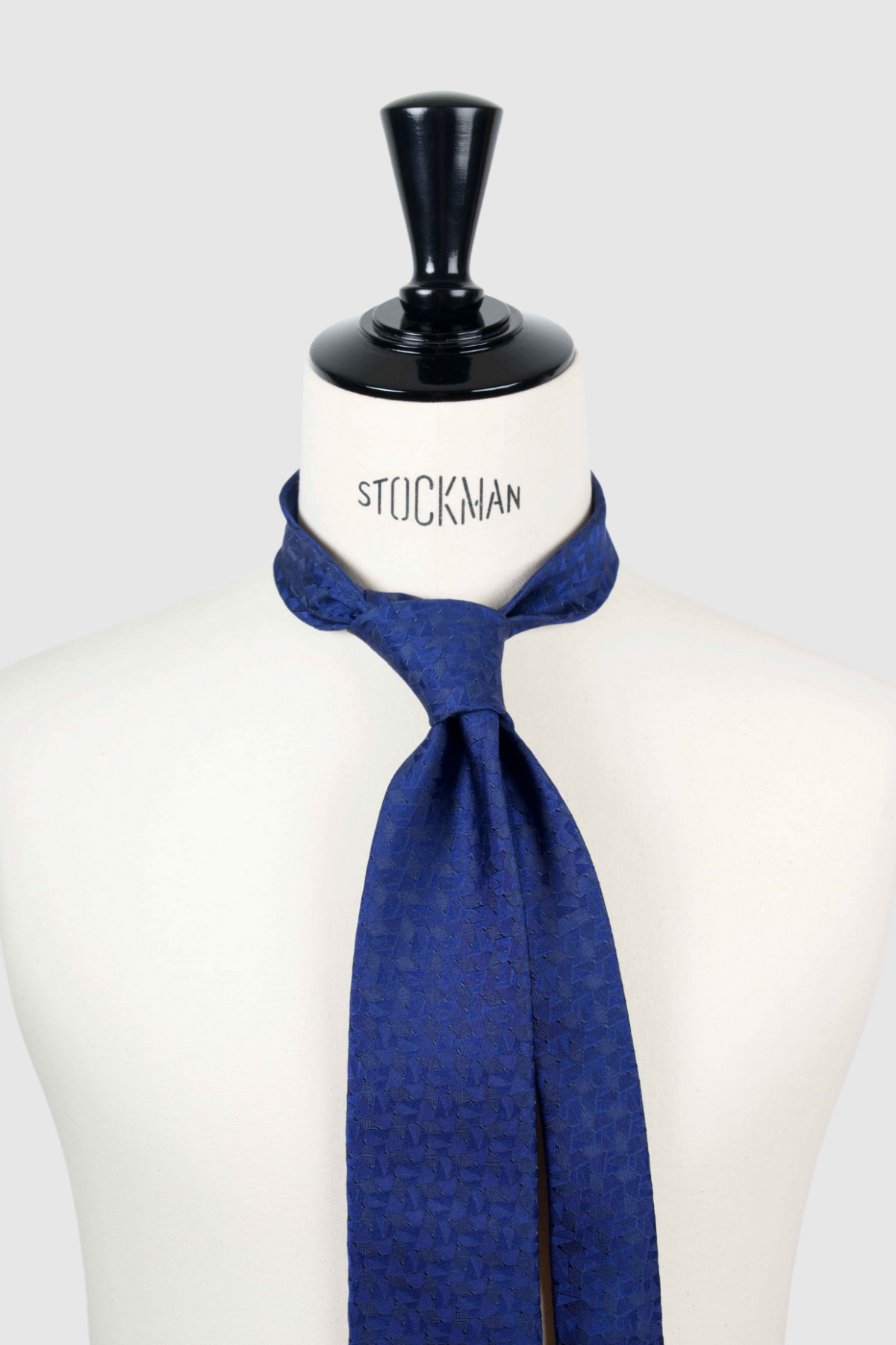 Cravate sartoriale à 3 plis, bleu marine profond, motif géométrique et aperçu du noeud simple sur buste Stockman.