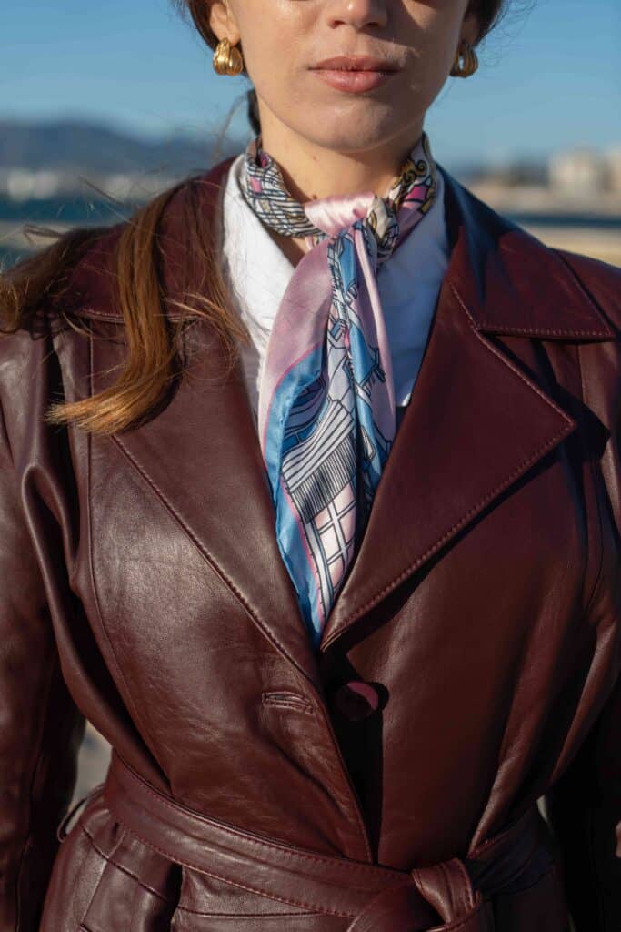 Carré de soie rose et violet plié en bande fine et noué au cou, porté sous un manteau en cuir bordeaux, Dare in Paris