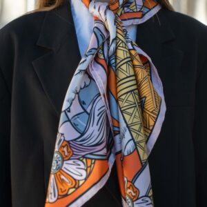 Carré de soie orange, L’envol des gourmandises, porté noué au cou sur une veste noire, Dare in Paris
