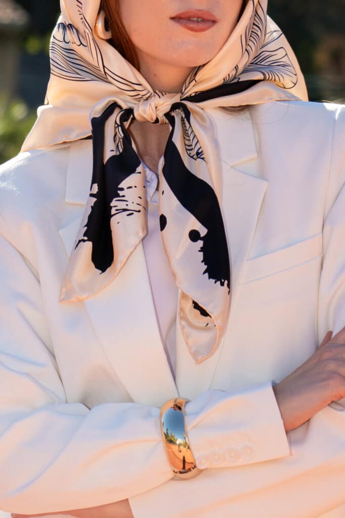 Carré de soie noir et blanc cassé noué en foulard de tête sous le menton, porté avec un tailleur blanc, Dare in Paris