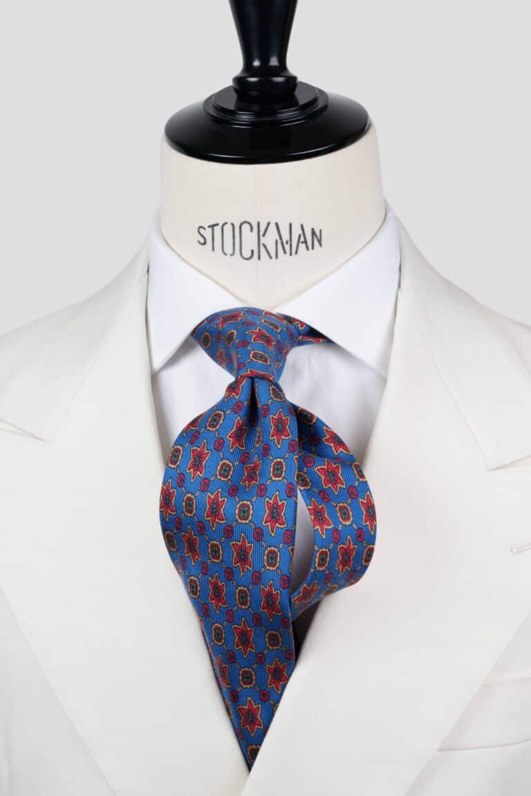 Cravate bleue à motif géométrique rouge et jaune, soie imprimée ancient madder 3 plis artisanale, nouée sur un buste, chemise blanche, Dare in Paris