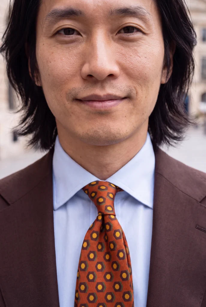 Dark brown seven-fold madder silk tie, worn with a shirt and jacket, close-up view.