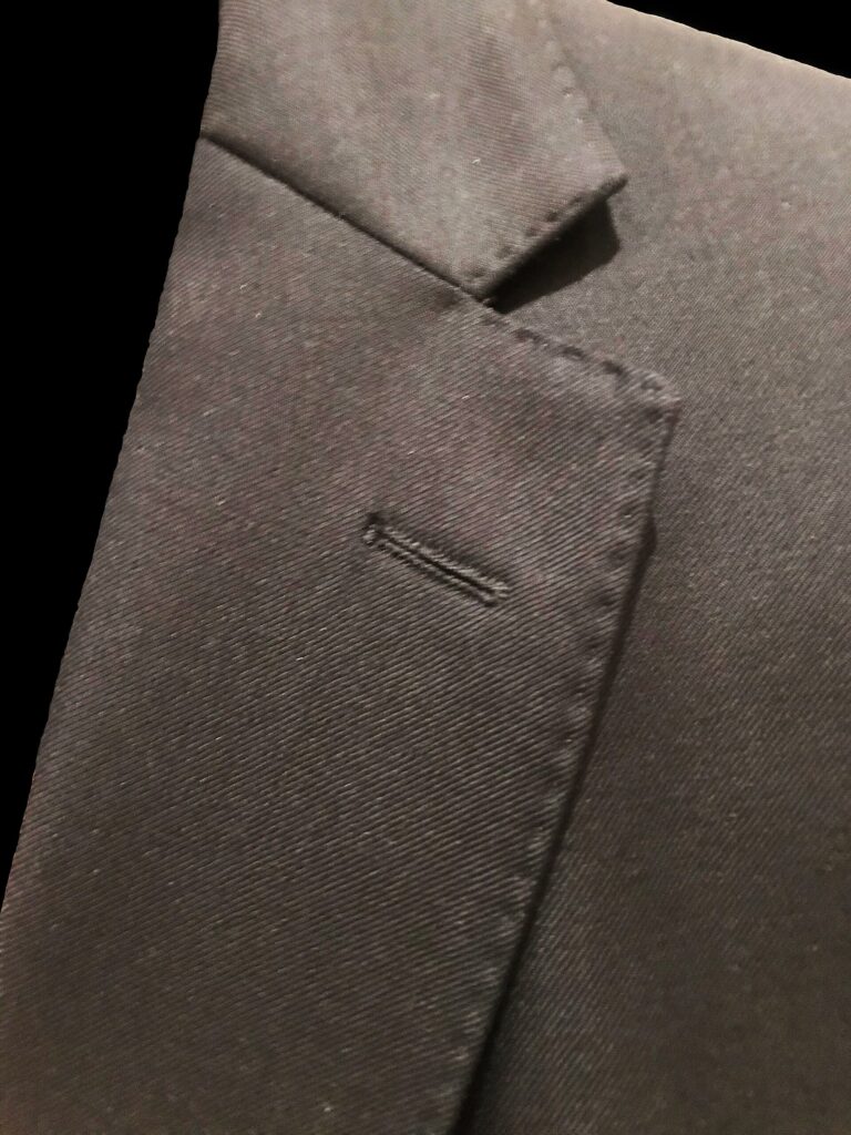 Gros plan sur le revers cranté d'une veste de costume sombre, avec boutonnière et surpiqûres visibles
