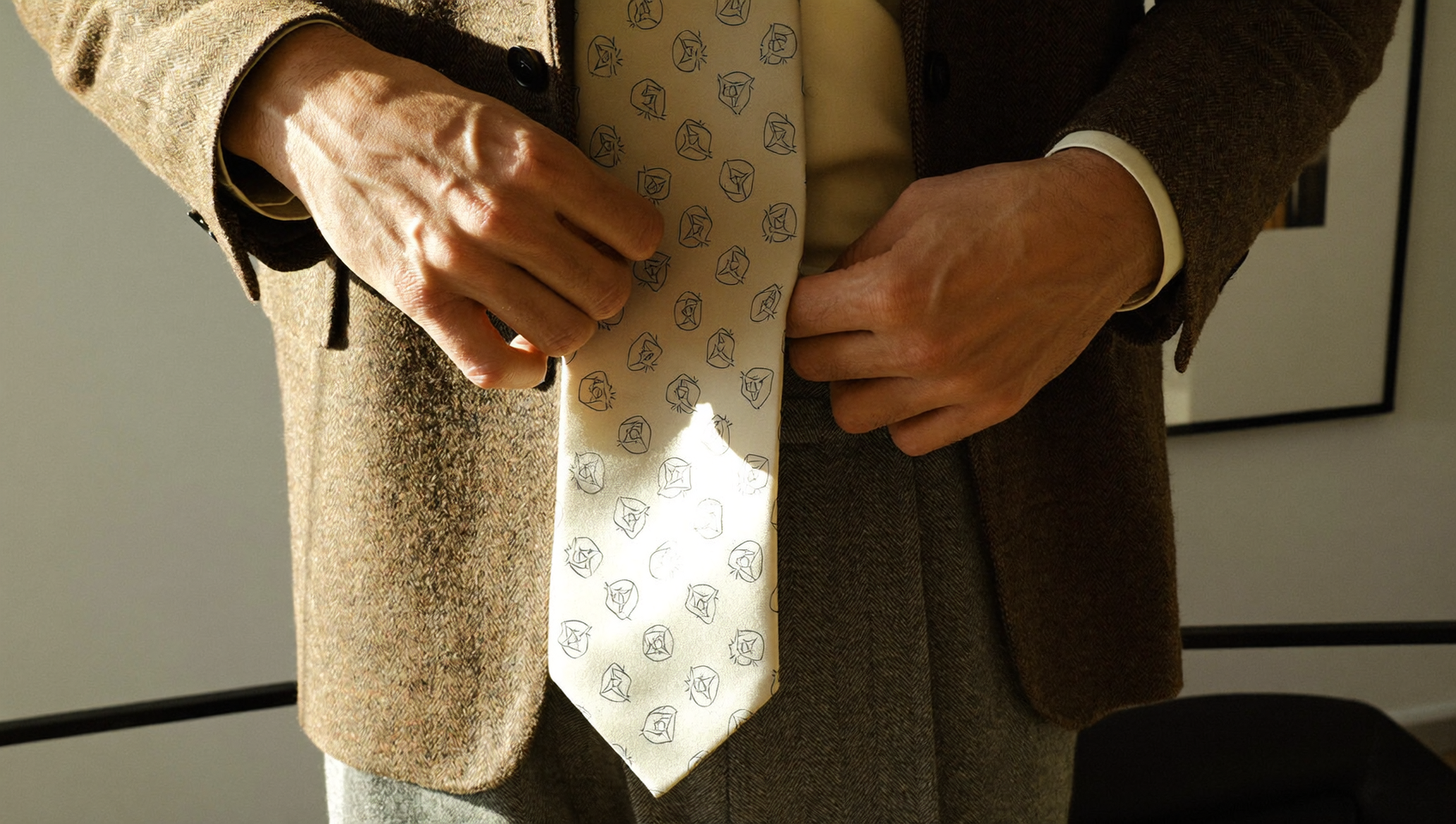 Homme ajustant sa cravate en hiver, soie mate à petits motifs sur une veste en tweed, près d'une fenêtre