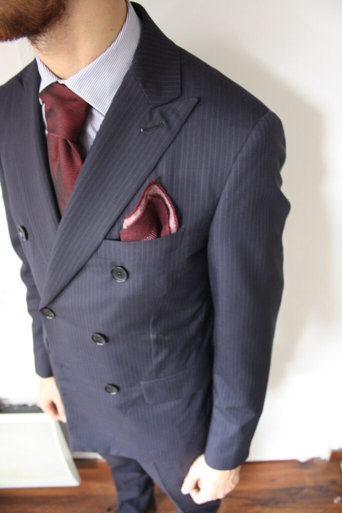 Homme en costume croisé bleu marine rayé portant une cravate grenadine bordeaux et une pochette assortie, visage hors cadre